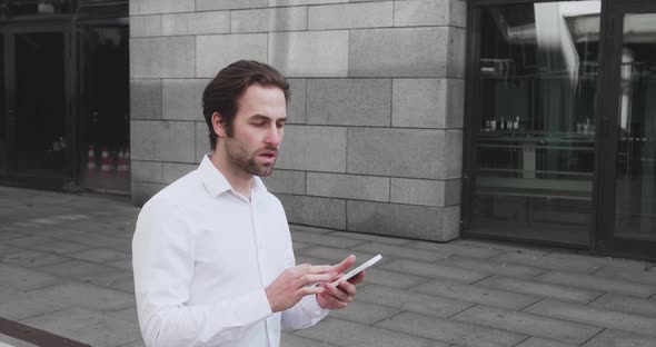 Young Man Texting Messages Cheating on His Smartphone While Walking in Office District