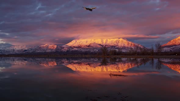 Airplane flying through the sky during colorful sunset with snow capped mountain