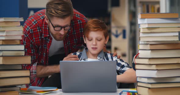 Teacher Helping Teen Schoolboy at Computer Terminal in Library