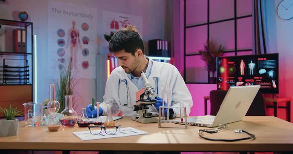 Chemist in Medical Uniform and Gloves Looking through Microscope on Biological Samples