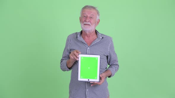 Happy Senior Bearded Man Thinking While Showing Digital Tablet