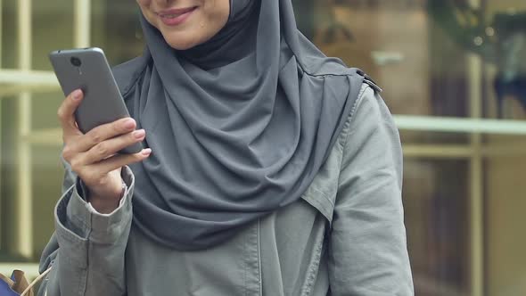 Arab Woman Typing Message on Smartphone, Boasting to Friends About Purchases