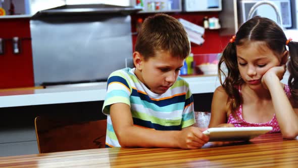 Siblings using digital tablet in kitchen