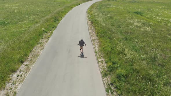 Man Rides at Straight Road on Longboard at Sunset Time Aerial . The Guy Rides a Longboard on the Way