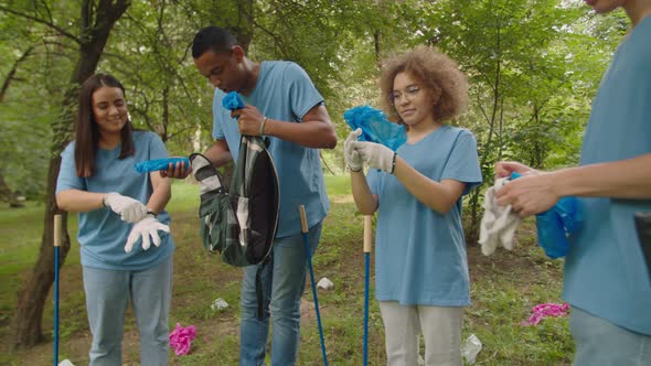 Mixed Race Male Leader Handing Out Garbage Bags to Friends Outdoors