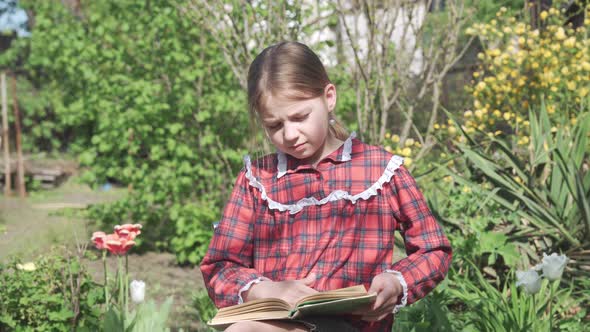 A Schoolage Girl Reads a Book in the Garden