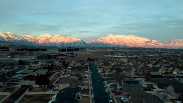 Suburban neighborhood with Silicon Slopes at Lehi, Utah at sunset - pull back aerial flyover