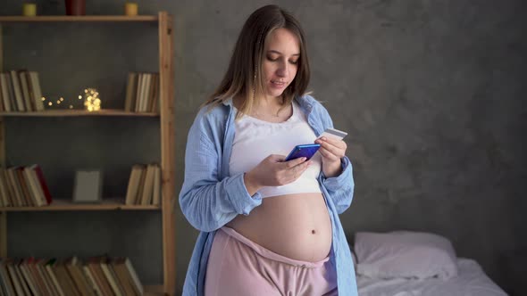 Young Pregnant Woman Shopping on Internet Using Banking App or Service on Smartphone and Credit Card