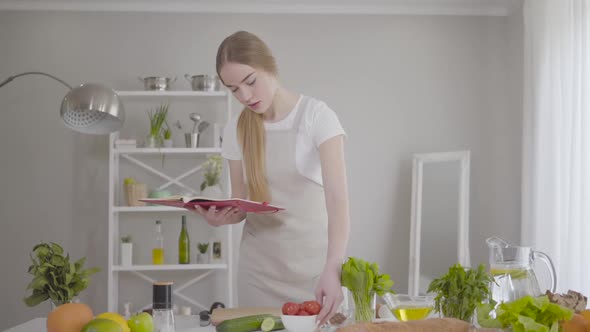 Portrait of Serious Concentrated Caucasian Woman Looking at Ingredients at the Table and Reading