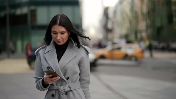 Adult Busy Woman is Walking on Street in Downtown and Reading Meaasge in Smartphone