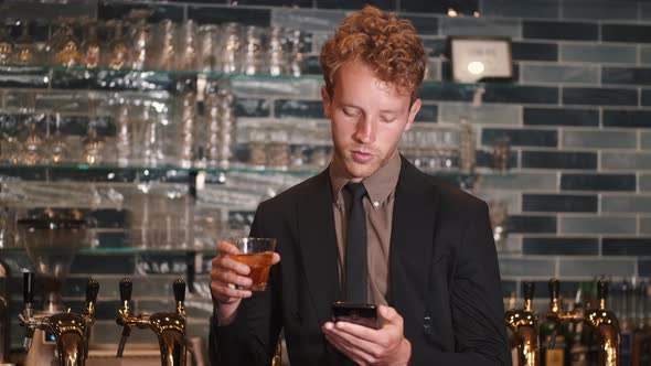 Young Businessman Sitting in a Bar Reading Smartphone Texts