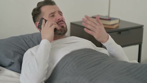 Angry Man Talking on Smartphone in Bed