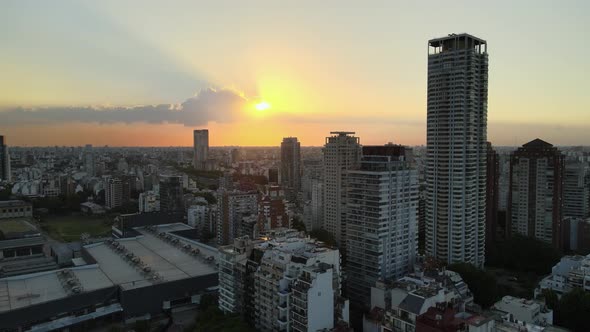 Pan left flying over Palermo neighborhood buildings and skyscraper at sunset with sun shining behind