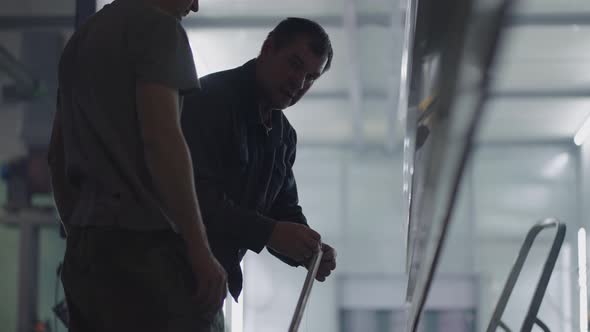 Two Male Painters Prepare Steel Metal Elements for Painting By Fixing Them on Suspensions