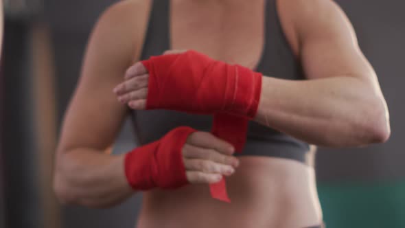 Mid section of caucasian female boxer wrapping boxing tape on her hands at the gym