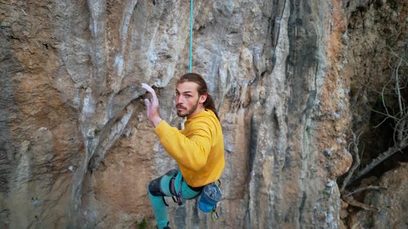 Slow Motion of Joyful Handsome Man Rock Climber in Yellow Sweatshirt with Long Hair Hanging on Rope