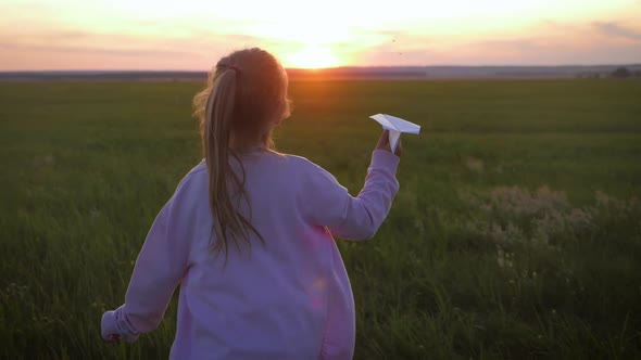 Happy Little Girl Playing with a Paper Airplane Outdoors During Sunset. Concept Big Child Dream.