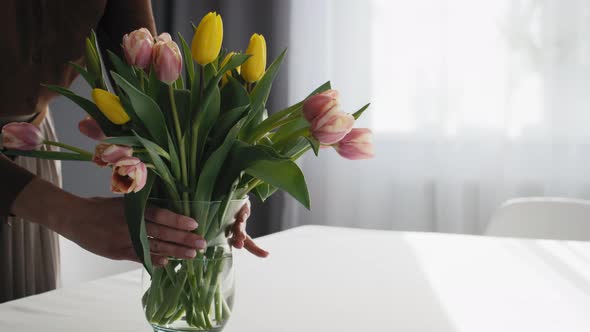 Caucasian woman putting fresh tulips in the vase on the table. Shot with RED helium camera in 8K.