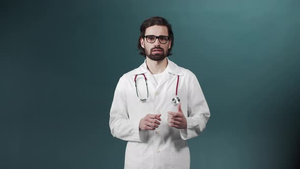 Young Medical Doctor in Glasses and with Statoscope Wearing White Coat in a Green Room Talks About