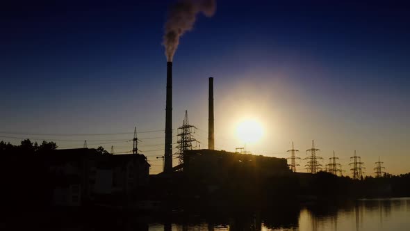 Silhouette of factory at sunset. Dark smoke from industrial pipe filling the air. 