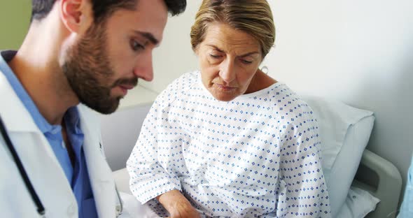 Male doctor discussing medical report with female patient on digital tablet