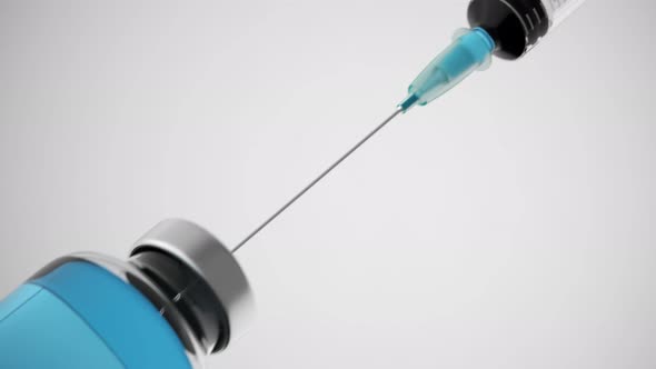 Long syringe needle drawing blue liquid from a container on a bright background.