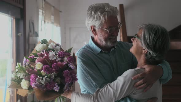 Portrait of couple of two happy and in love seniors or mature and old people holding flowers at home