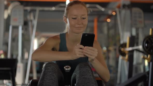 Slowmotion Shot of a Young Woman at the Gym Shakes the Press Holding the Phone in Front of Her Eyes