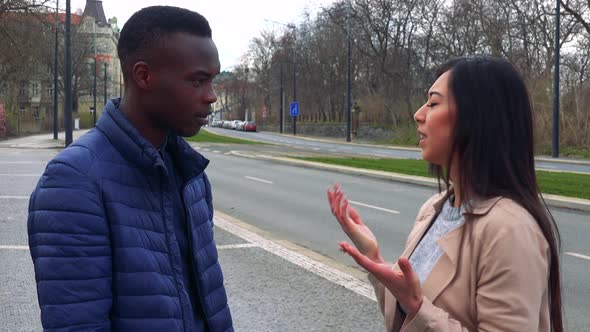 A Young Black Man and a Young Asian Woman Argue in a Street in an Urban Area