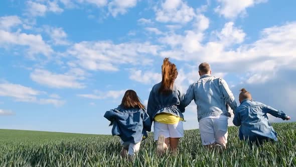 Mom Dad and Two Children Run Happily Among the Fields Against the Blue Sky