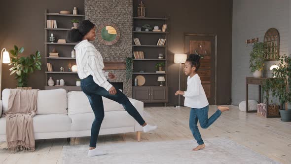 Carefree African Mom with Child Preteen Daughter Having Fun Together in Living Room Dancing to Music