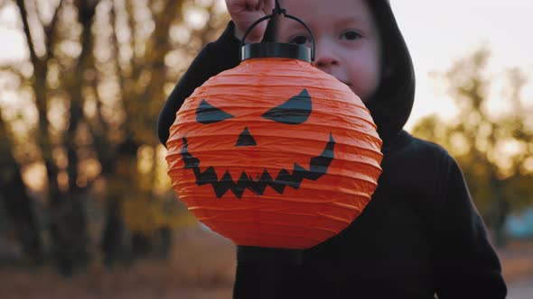 Little Boy Having Fun with Halloween Carved Pumpkin in a Park at Dusk. Halloween, Holiday and