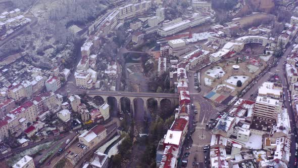Drone pull back from iconic bridge in heart of small town Saint-Claude. Snowy cityscape of France