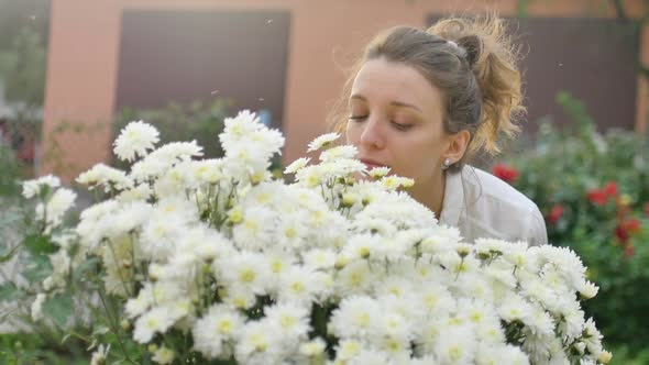 Pretty Young Girl Is Standing Near a Bush of White Chrysanthemums in Park During Spring Time