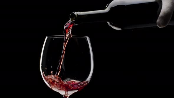 Red wine is pouring into a glass on a black background. Close shot.