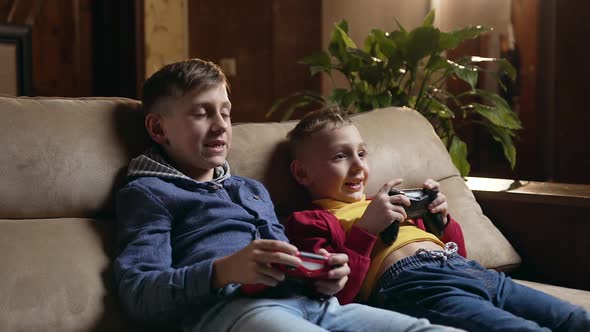 Schoolboys Sitting on the Soft Couch at Home and Playing Video Games with Joysticks