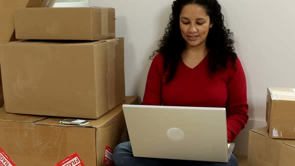 Woman sitting by unpacked boxes with laptop