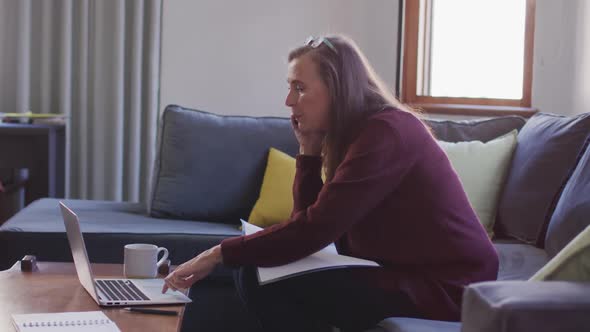 Woman talking on smartphone while using laptop at home