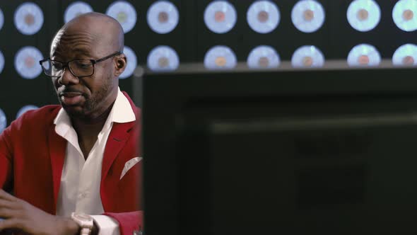 Bald Africanamerican Businessman in Red Suit Speaks to Someone on Smartphone