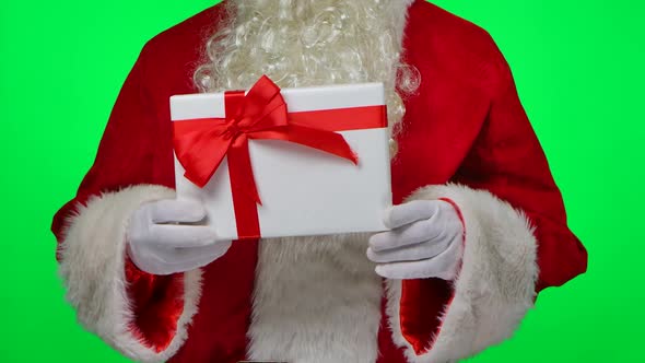 Santa Claus with Beard in White Gloves and a Red Suit Holding a Gift Box in His Hands