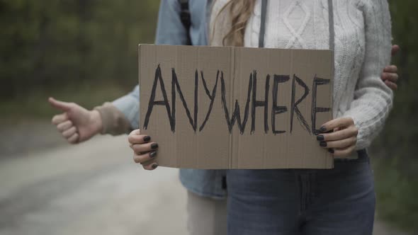 Unrecognizable Young Woman Holding Anywhere Sign with Blurred Man Showing Thumb Up at Background