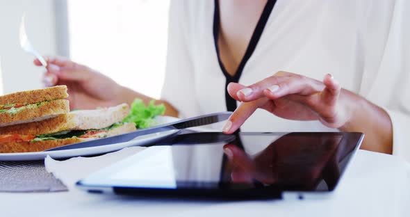 Woman eating lunch and using tablet computer