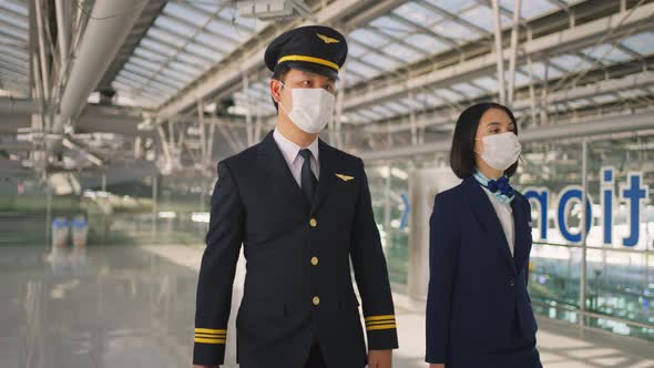 Airliner pilot and air hostess wear face mask walking in airport terminal to airplane during Covid19