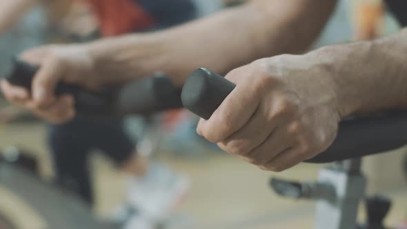 Close-up of Male Caucasian Hands Putted on Handlebar of Exercise Bike in Gym. Unrecognizable Young