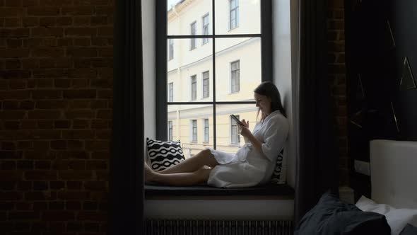 Woman in Bathrobe Using Smartphone on Windowsill