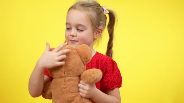 Adorable Little Girl Hugging Teddy Bear Standing at Yellow Background