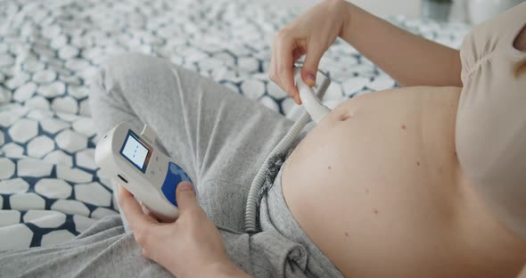 Young Pregnant Woman Using Pocket Ultrasound Doppler to Check Baby Heart Rate