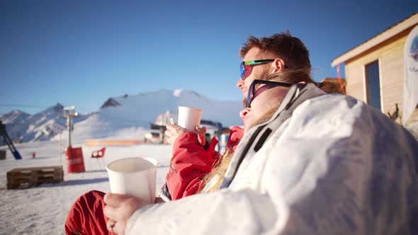 Smiling Caucasian Female Sitting with Male in Glasses with Head on His Shoulder in Ski Mountain