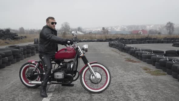 Portrait of Brutal Man on Motocycle Looking Aside Near Tires