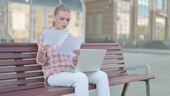 Young Woman Reacting to Loss While Reading Documents and Working on Laptop Outdoor